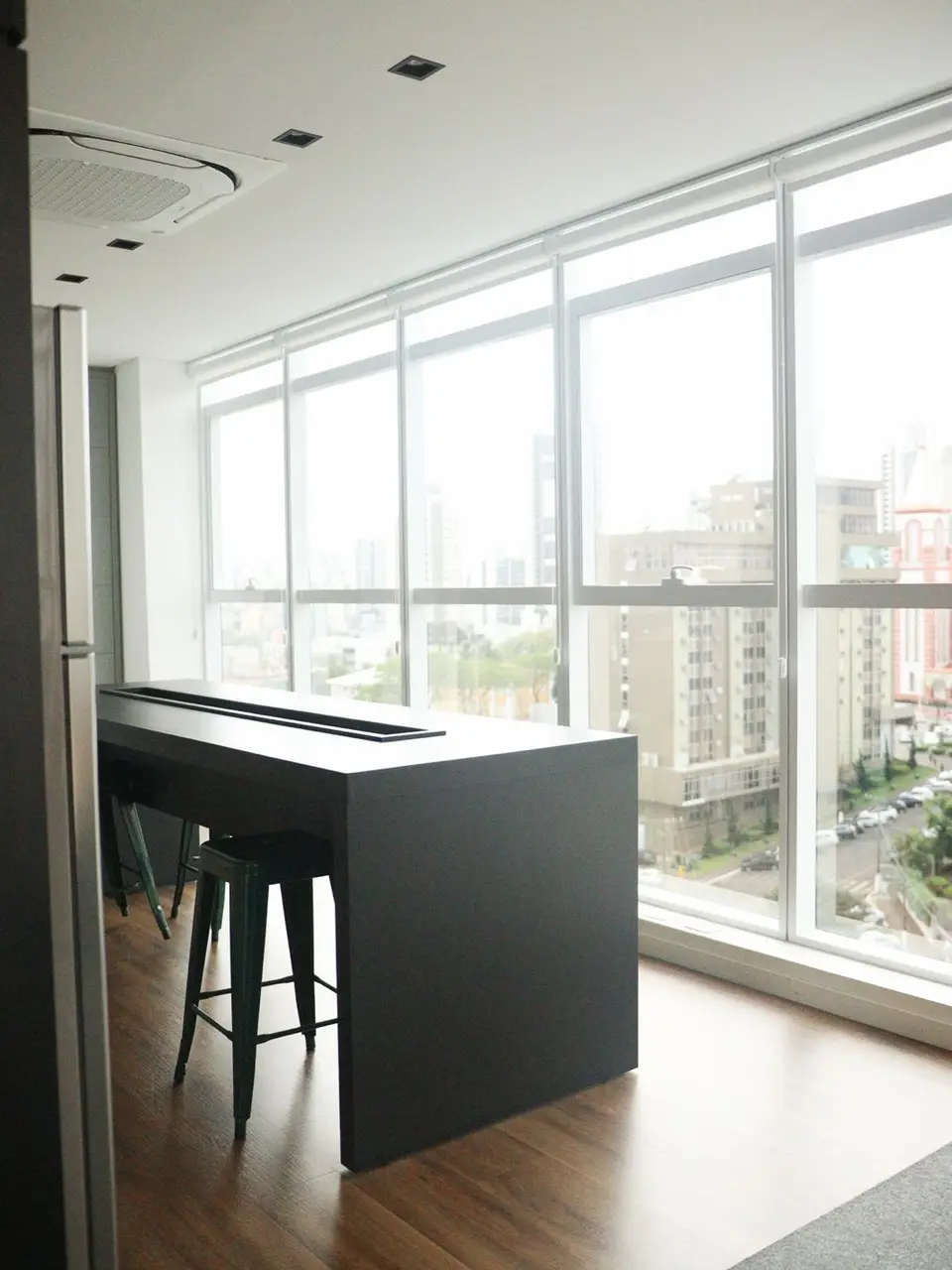 Bancada preta com banquetas diante da parede de vidro com vista para o Centro de Chapecó.