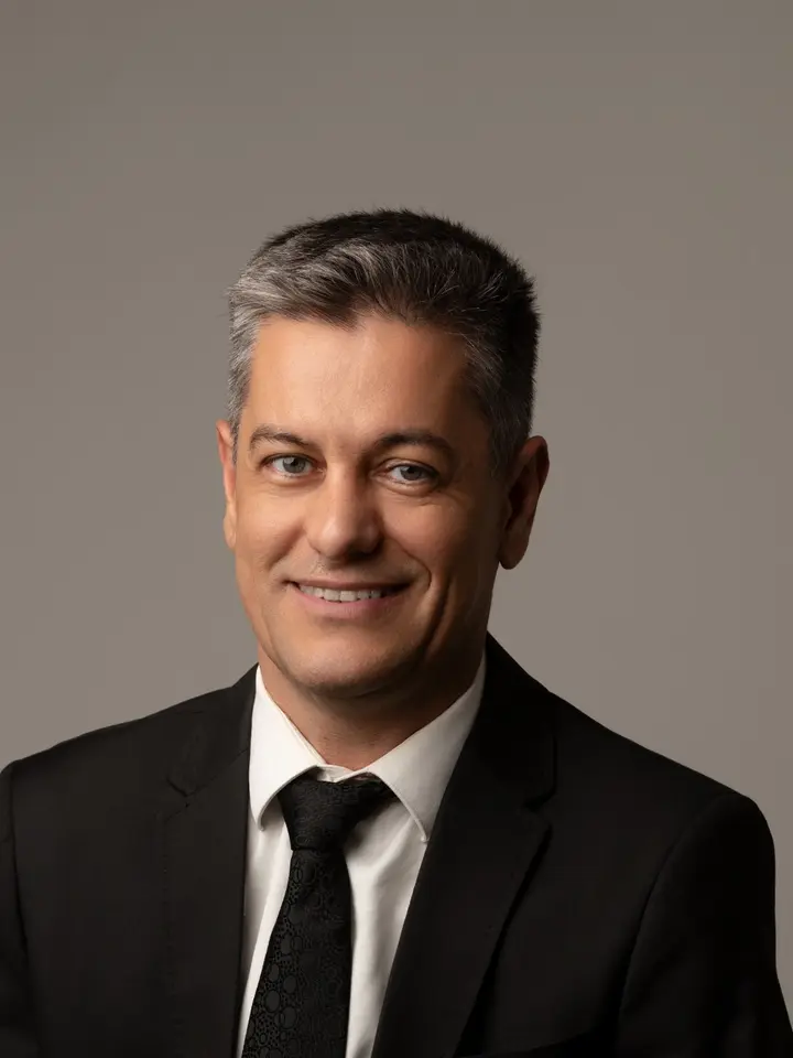 Vinicius Romanini, de terno escuro e gravata, em retrato com fundo cinza.